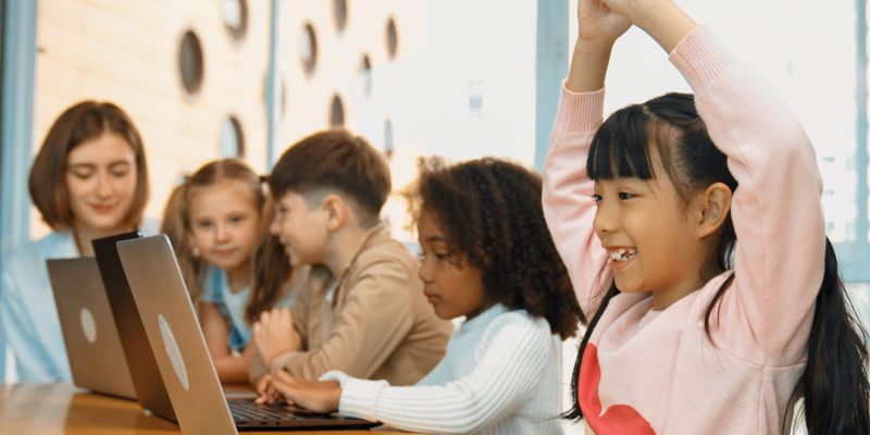 Asian girl working on laptop and stretch arms to relax body. Diverse children coding or programing engineering code or prompt by using computer in STEM class while teacher explain system. Erudition.
